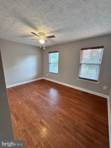 an empty room with wooden floor chandelier fan and windows
