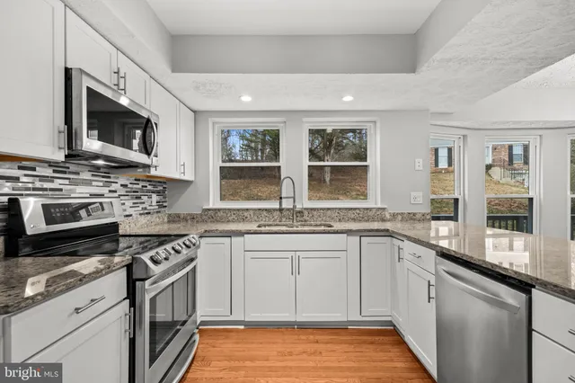 a kitchen with stainless steel appliances granite countertop a stove top oven a sink dishwasher a dining table and chairs with wooden floor