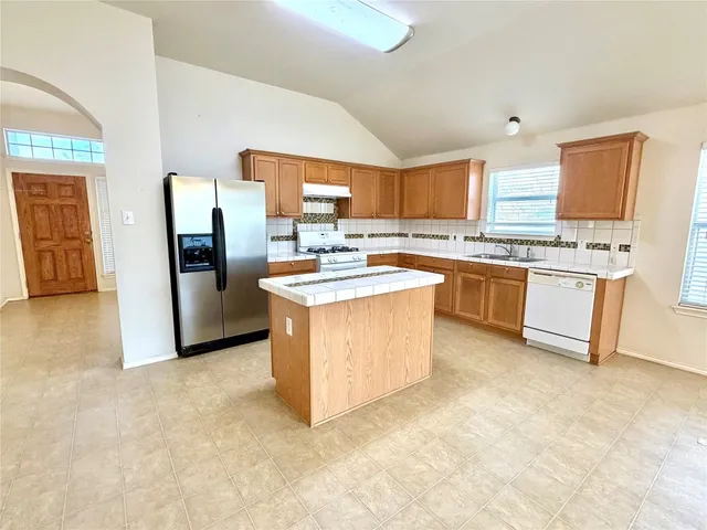 a kitchen with stainless steel appliances granite countertop a stove top oven a sink a refrigerator and white cabinets