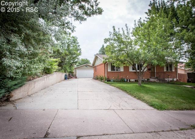 2007 North Chelton Road Colorado Springs, CO 80909 - Photo 2 of 35 Featuring a large driveway and green front yard with mature trees.