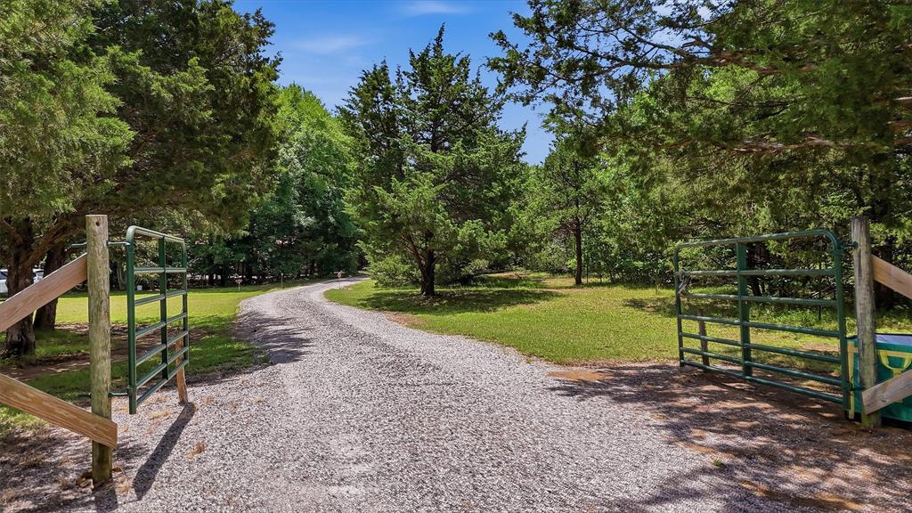 3958 Ranch Road Whitesboro, TX 76273 - Photo 36 of 40 Gravel driveway with surrounding mature trees, featuring a green metal gate and wooden fence posts