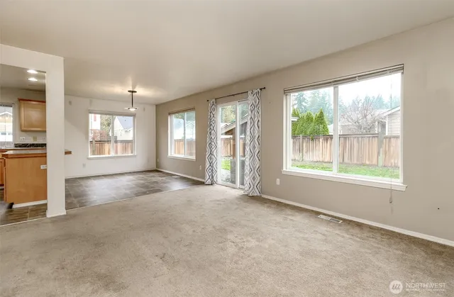 an empty room with windows and view of kitchen