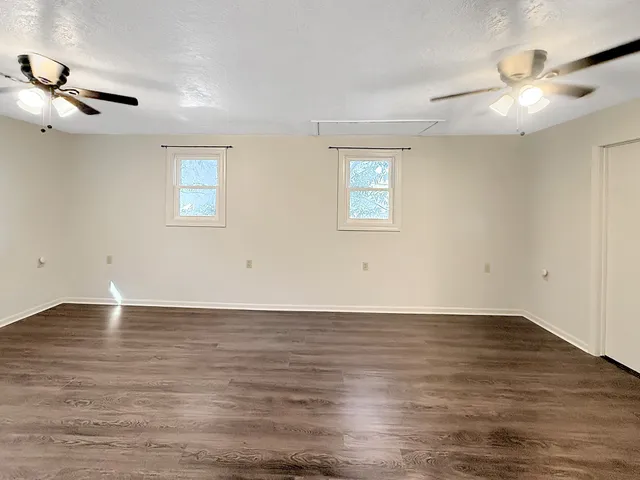 an empty room with wooden floor chandelier fan and windows