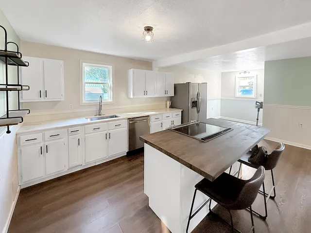 a kitchen with a stove a sink dishwasher a dining table and chairs with wooden floor