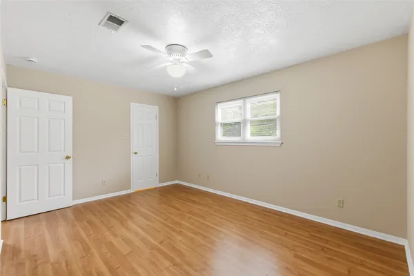 an empty room with wooden floor fan and windows