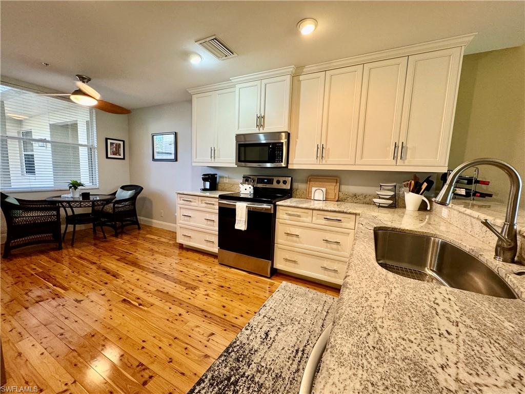 a kitchen with granite countertop a stove top oven a sink dishwasher and white cabinets with wooden floor