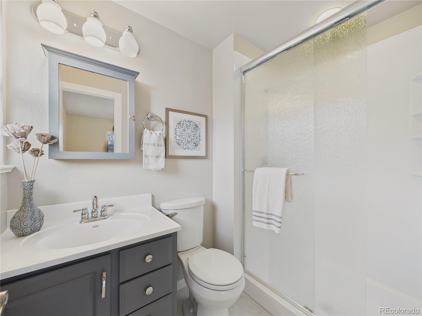 6085 Simms Street Arvada, CO 80004 - Photo 10 of 32 a bathroom with a toilet a sink a mirror and vanity