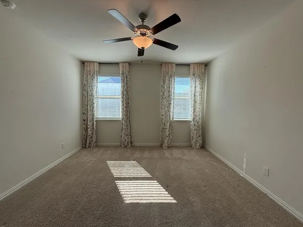 an empty room with ceiling fan and windows