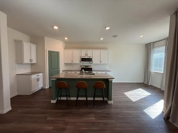 a open kitchen with stainless steel appliances granite countertop a stove a sink a refrigerator and white cabinets with wooden floor