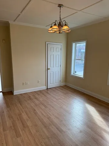an empty room with wooden floor chandelier and windows