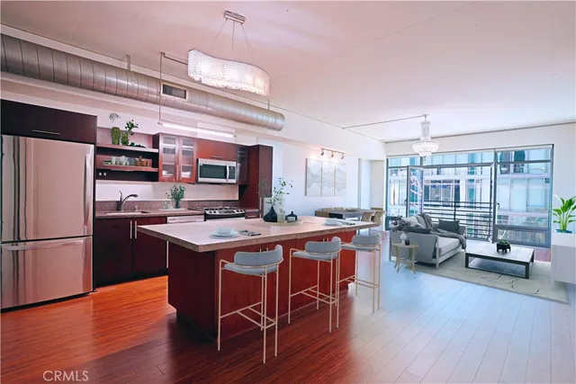 a kitchen with stainless steel appliances a stove a sink dishwasher a refrigerator white cabinets wooden floor and a dining table