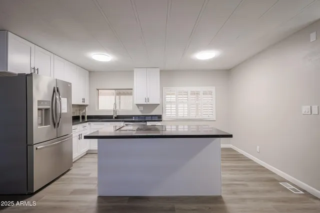 a kitchen with stainless steel appliances granite countertop a refrigerator a sink dishwasher a stove and white countertops with wooden floor