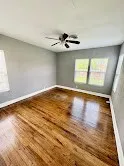 an empty room with wooden floor chandelier fan and windows