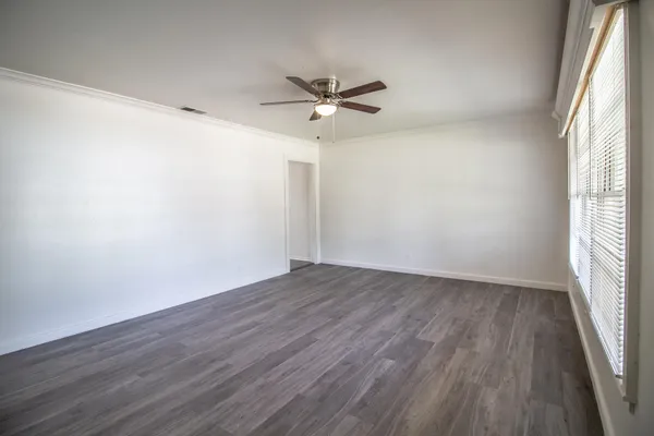 an empty room with wooden floor fan and windows