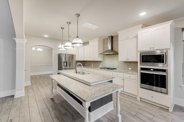 a large white kitchen with granite countertop a stove oven a sink dishwasher and a refrigerator with wooden floor