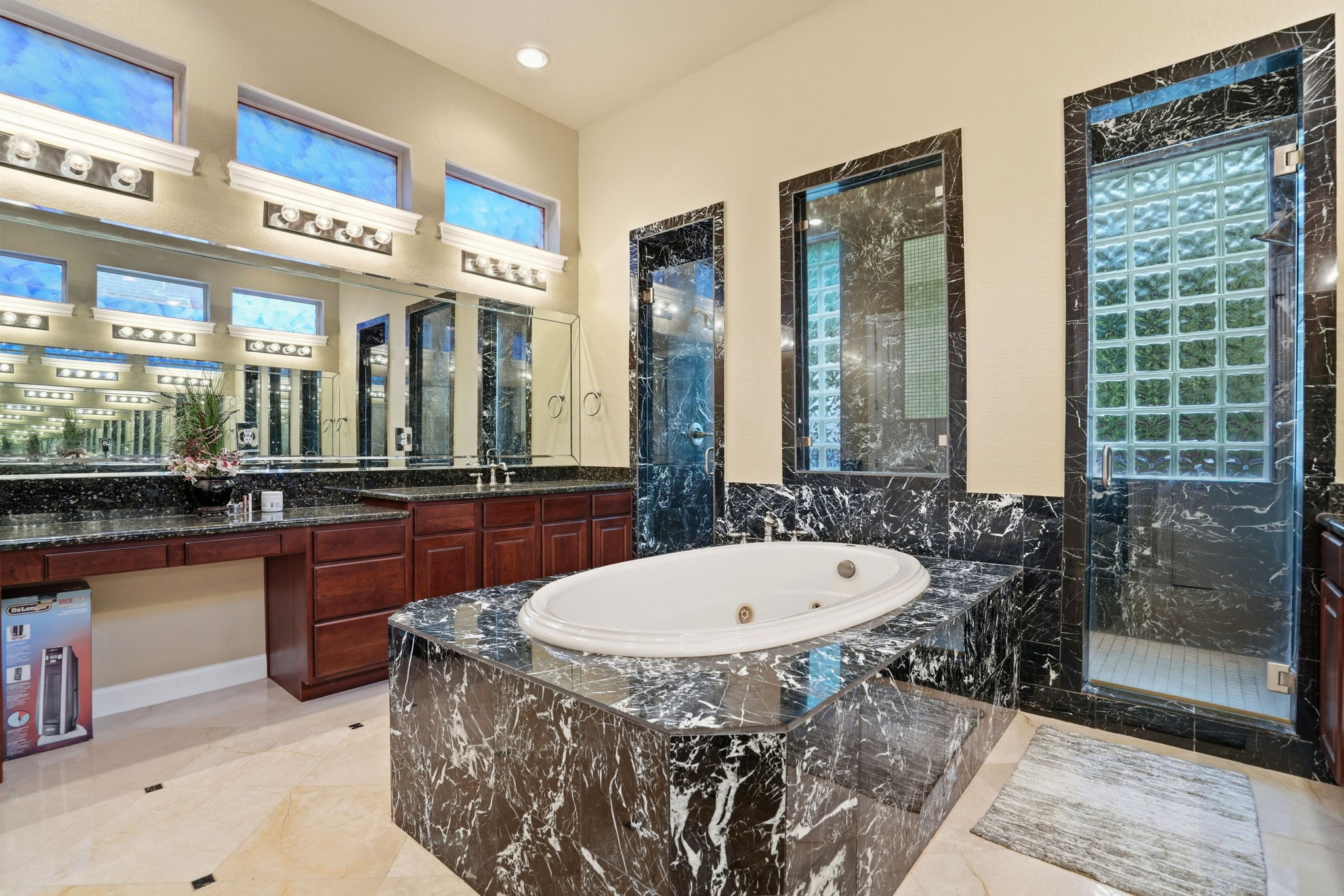 222 Vailco Lane Austin, TX 78738 - Photo 34 of 39 Built-in jetted tub with polished black stone surround, dual vanity with undermount sinks and wood cabinetry, expansive wall mirrors, and a glass-enclosed shower featuring glass block elements