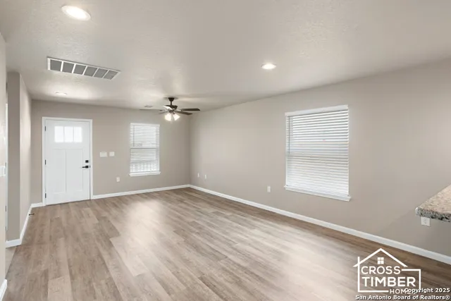 an empty room with wooden floor ceiling fan and windows