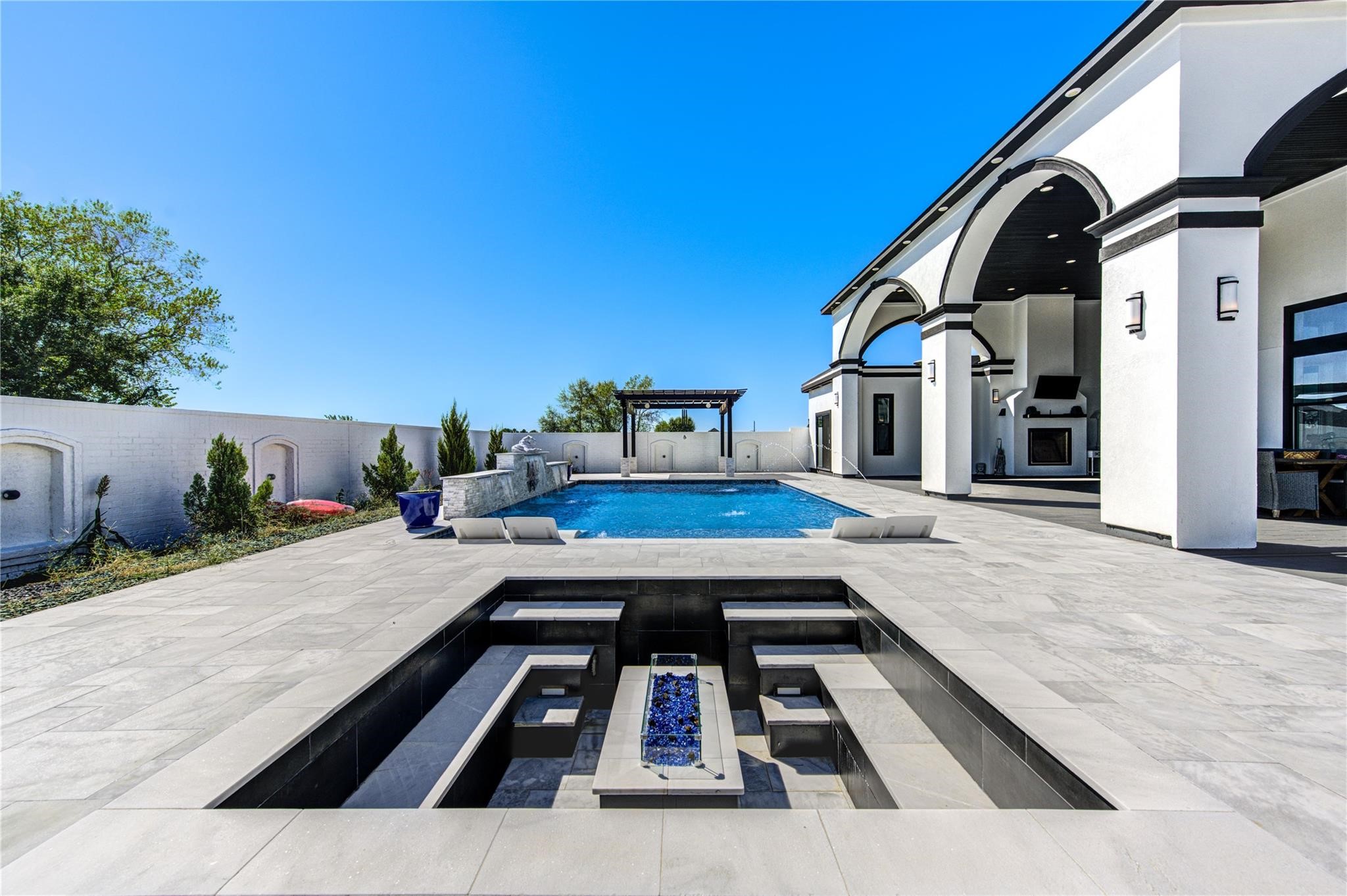 4821 Walters Road Richmond, TX 77469 - Photo 45 of 50 This stunning heated luxury pool creates a true resort-style experience with sleek modern design, expansive lounging areas, and breathtaking sunset views. Featuring elegant marble-style decking, in-water chaise loungers, ambient accent lighting, and a striking stone water feature, the space was thoughtfully designed for both relaxation and entertaining. A covered pergola lounge adds the perfect setting for evening gatherings, while the oversized pool offers a seamless blend of comfort & privacy.