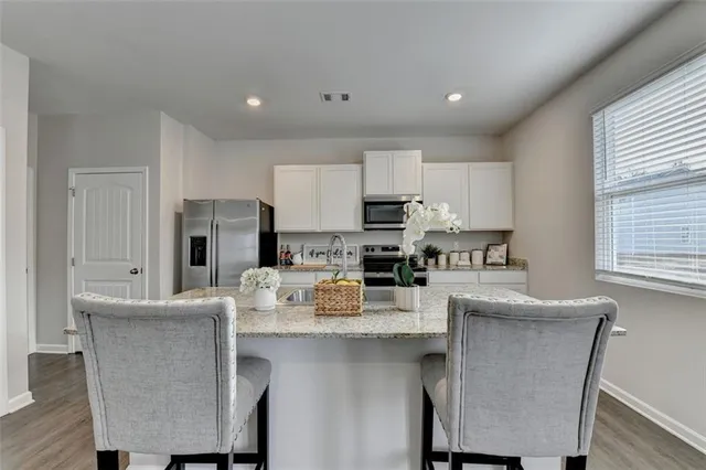 a kitchen with stainless steel appliances a stove a sink a refrigerator white cabinets and wooden floor