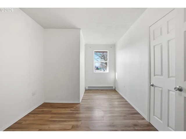 a view of an empty room with a window and wooden floor