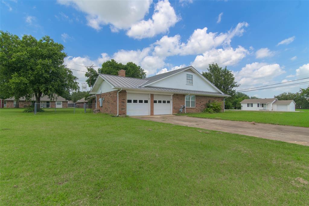 301 East 6th Street Krum, TX 76249 - Photo 27 of 29 Brick exterior with a metal roof, featuring a two-car garage with white panel doors