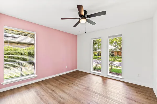 an empty room with wooden floor fan and windows