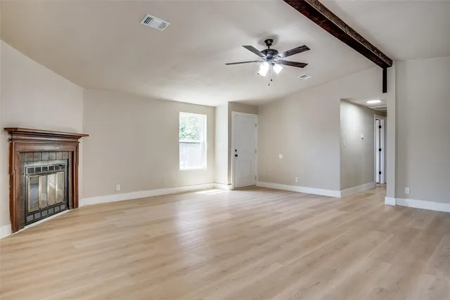 a view of an empty room with wooden floor and a ceiling fan