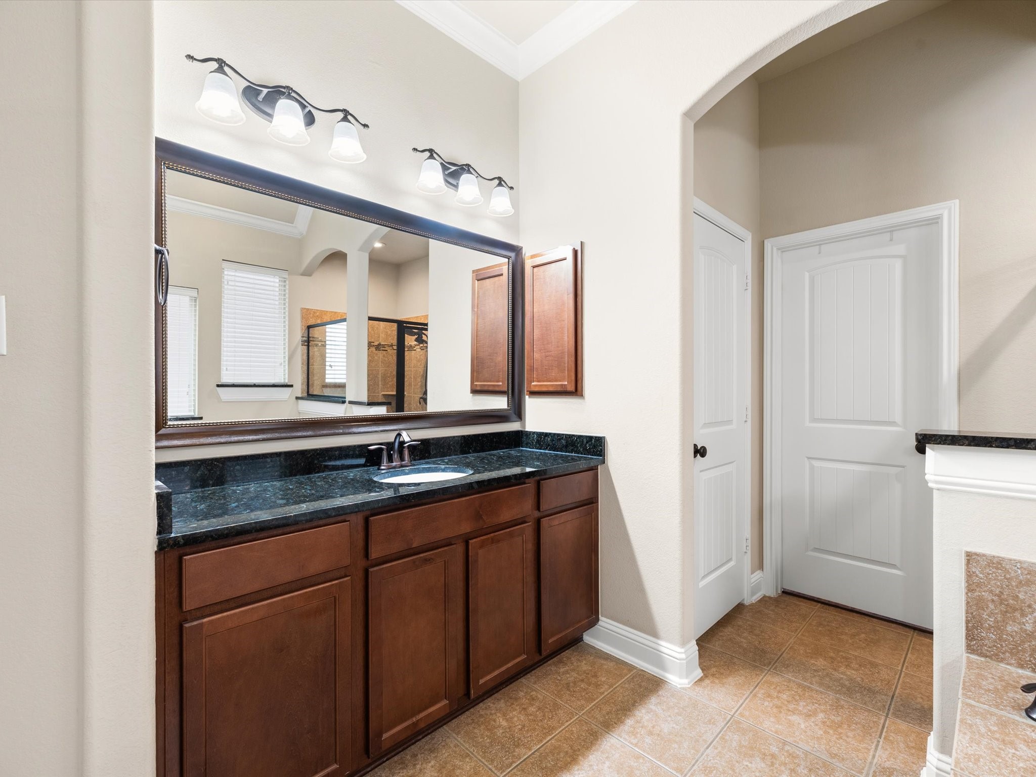 3907 Randle Ridge Court Fulshear, TX 77441 - Photo 19 of 46 This bathroom features two spacious vanities with dark granite countertops and rich wooden cabinets. It has elegant lighting fixtures, a large mirror, and neutral tile flooring, creating a modern and inviting atmosphere.