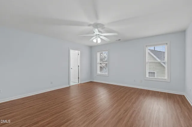 an empty room with wooden floor ceiling fan and windows