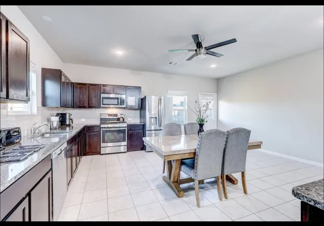 a kitchen with stainless steel appliances kitchen island granite countertop a dining table chairs refrigerator and microwave