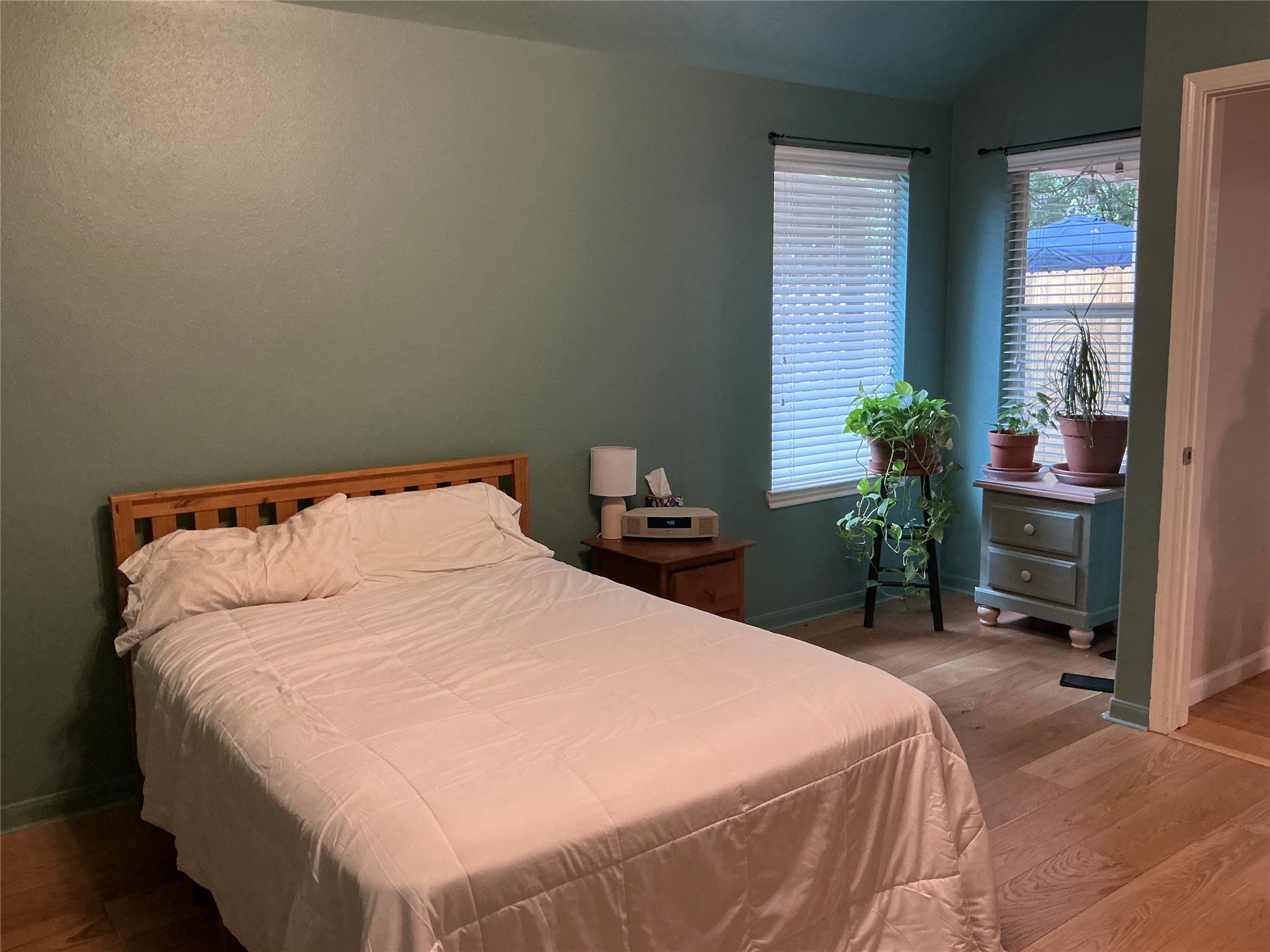 2910 Crescent Bend Road Spring, TX 77388 - Photo 12 of 29 Cozy bedroom with soft teal walls, hardwood flooring, and ample natural light from two windows. Features a comfortable bed, nightstand, and a small dresser with potted plants, creating a tranquil atmosphere.