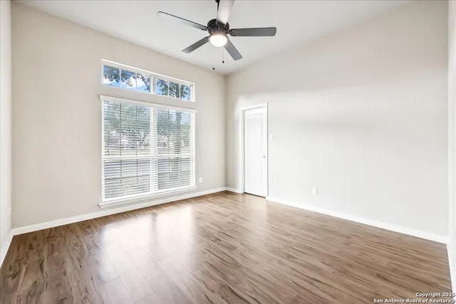 an empty room with wooden floor chandelier fan and windows