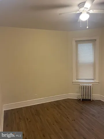 a view of an empty room with wooden floor and a fan