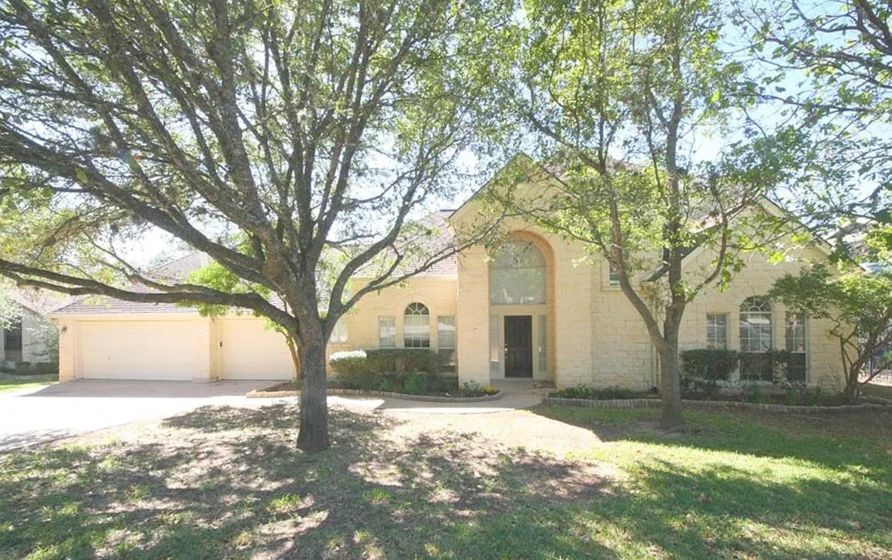 A cream-colored stone facade and mature trees create a welcoming curb appeal.