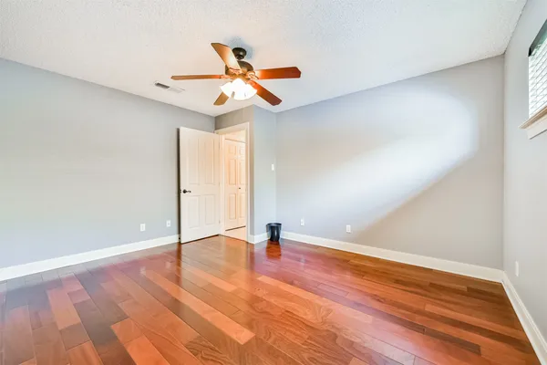 an empty room with wooden floor fan and windows