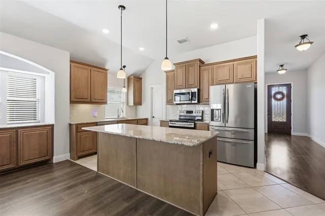 a kitchen with stainless steel appliances granite countertop a refrigerator a sink dishwasher a stove top oven a kitchen island and couches with wooden floor