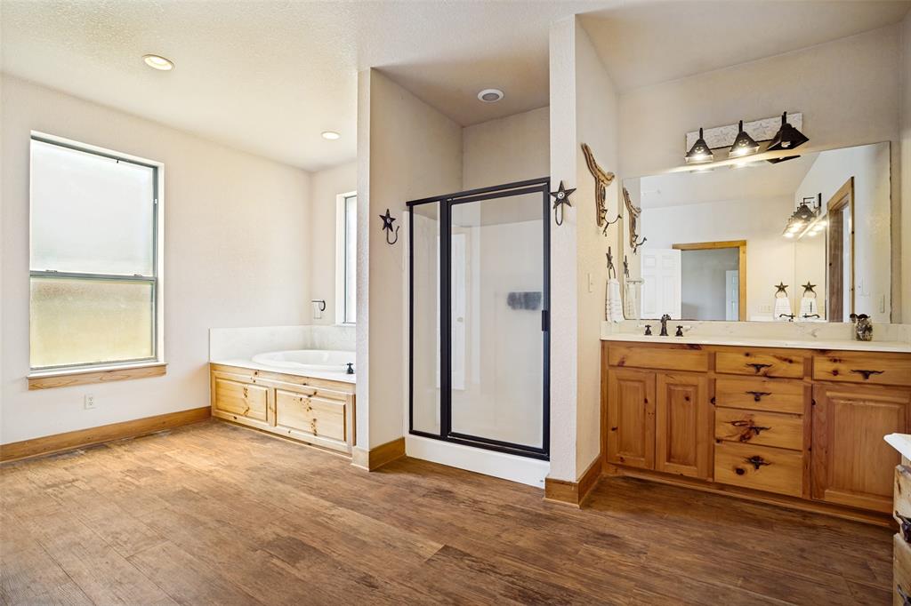 243 ROCK Court Decatur, TX 76234 - Photo 12 of 25 Spacious bathroom featuring wood-finish flooring, a soaking tub with a tiled surround and wood cabinetry, a glass-enclosed shower, and a double vanity with a large mirror and three-light fixture