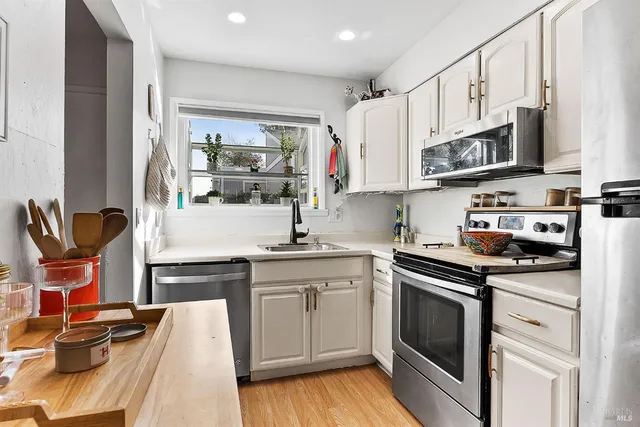 a kitchen with stainless steel appliances granite countertop a stove top oven a sink dishwasher and white cabinets with wooden floor