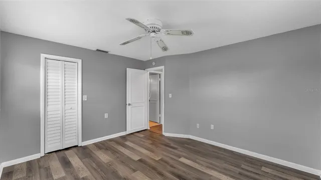 a view of an empty room with wooden floor and a ceiling fan