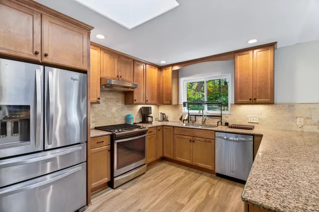 a kitchen with stainless steel appliances granite countertop a refrigerator a sink dishwasher a stove and white countertops with wooden floor