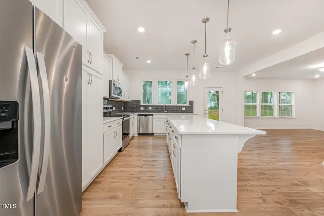 a kitchen with stainless steel appliances granite countertop a refrigerator a sink dishwasher a stove and a dining table with wooden floor