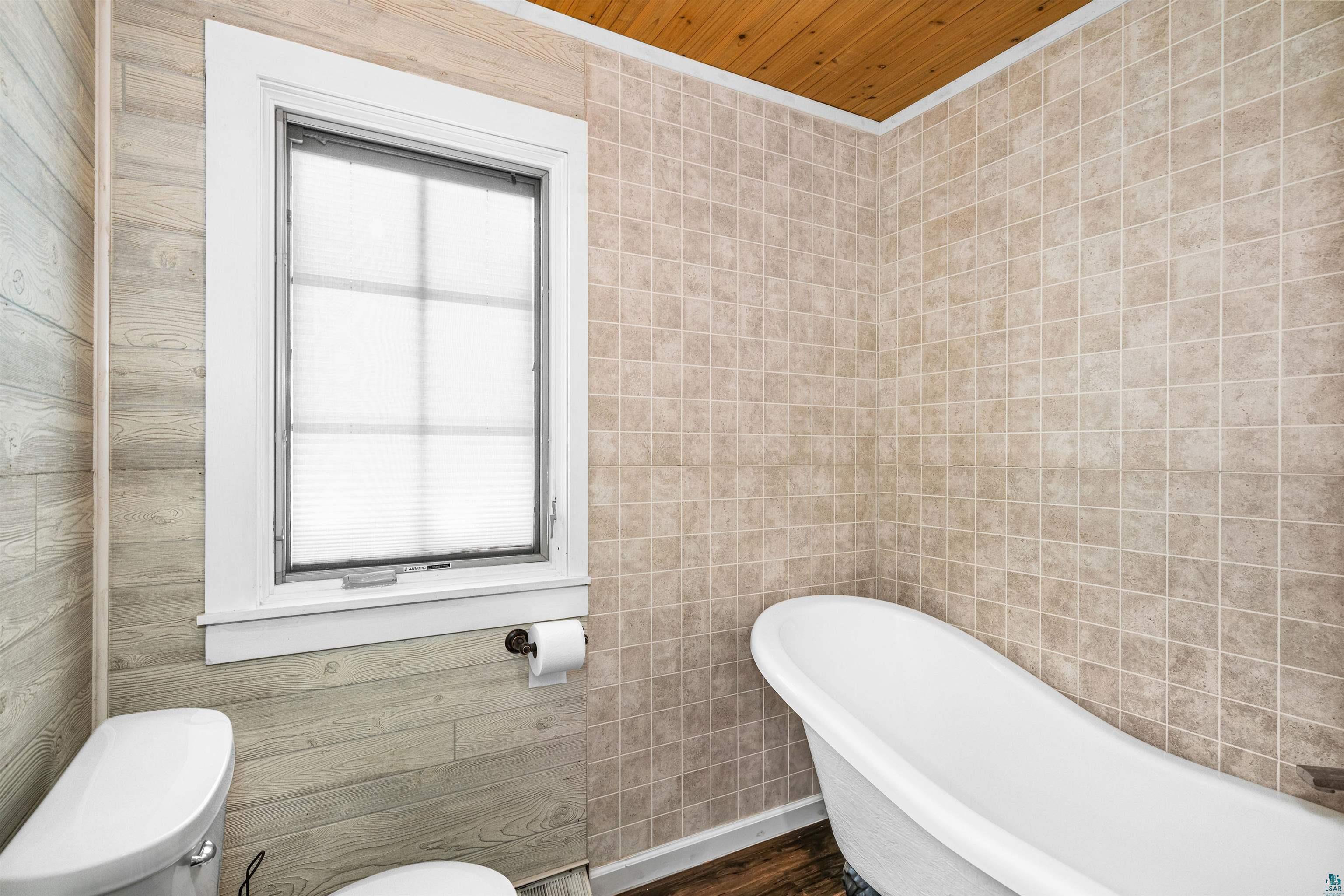 3325 Strand Road Duluth, MN 55803 - Photo 23 of 25 Bathroom featuring a standalone soaking tub, white framed window, wood-finish plank wall, neutral square tile, and wood-finish ceiling