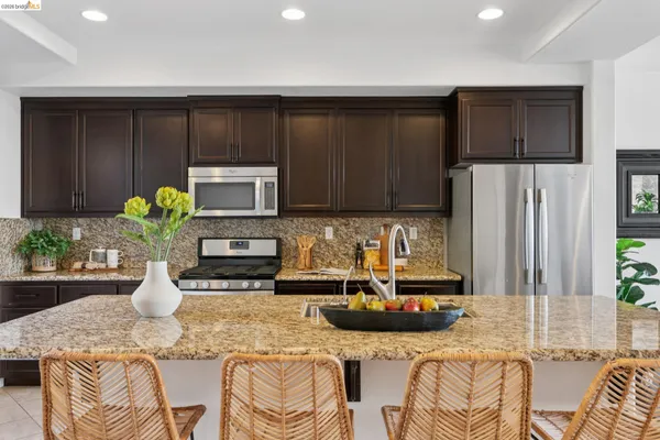 a kitchen with stainless steel appliances granite countertop a refrigerator a stove a sink a dining table and chairs