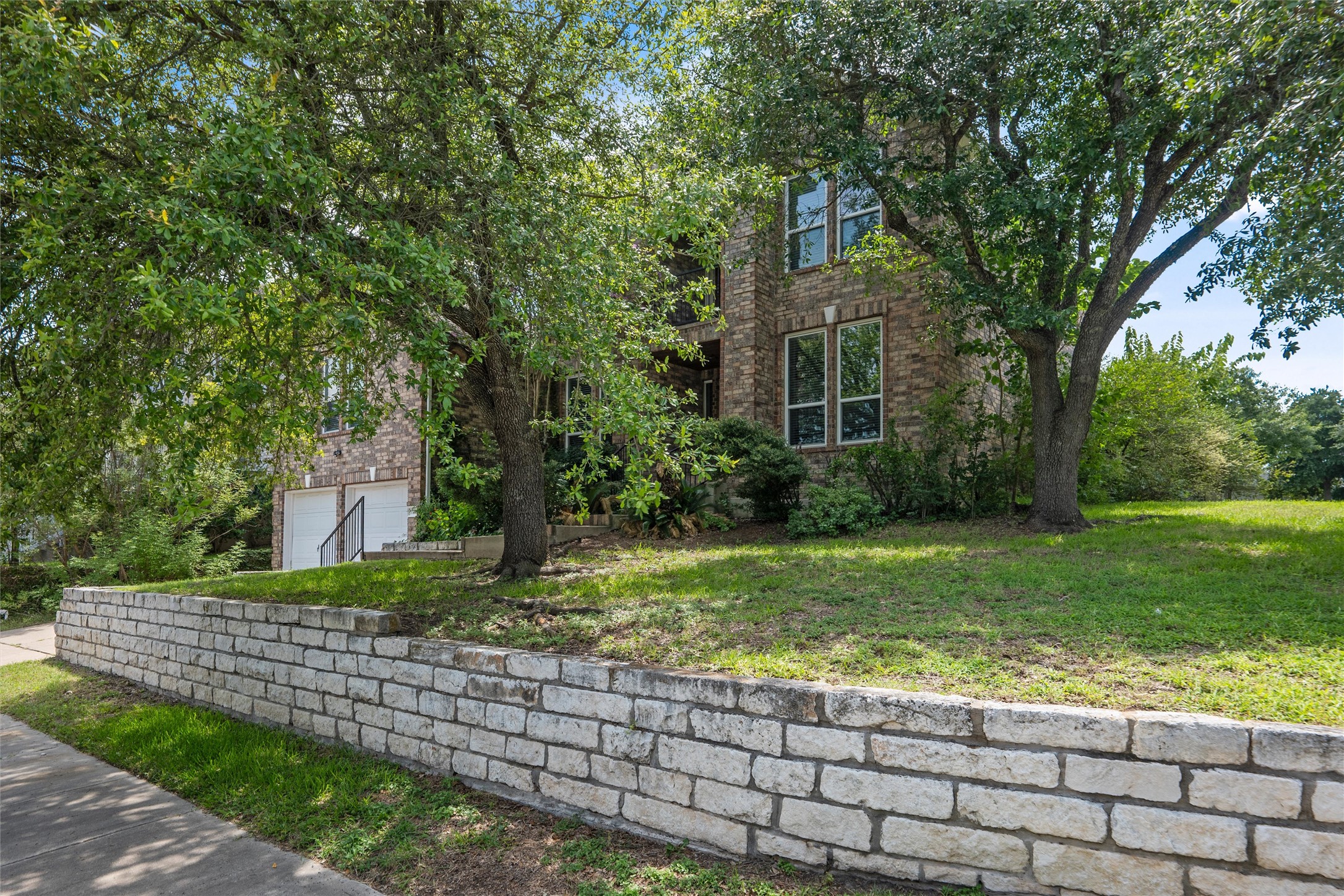 7000 Colberg Court Austin, TX 78749 - Photo 40 of 40 Mature trees frame a charming brick residence, set back on a verdant lawn behind a stone retaining wall.