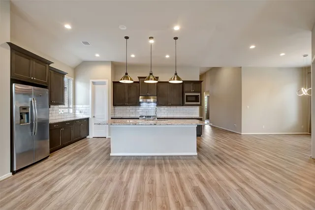 a large kitchen with stainless steel appliances kitchen island a large counter top and wooden floors