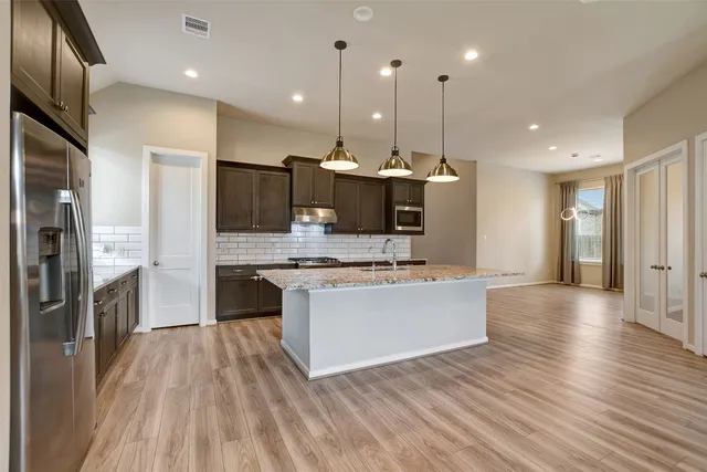 a large kitchen with stainless steel appliances a large counter top a stove a sink dishwasher and a refrigerator with wooden floor