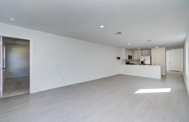 an empty room with kitchen view and a refrigerator
