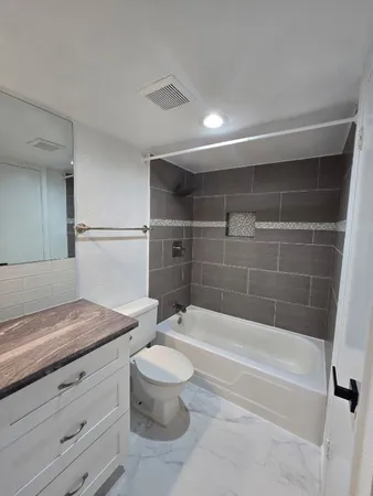 a bathroom with a granite countertop bathtub shower sink vanity and toilet