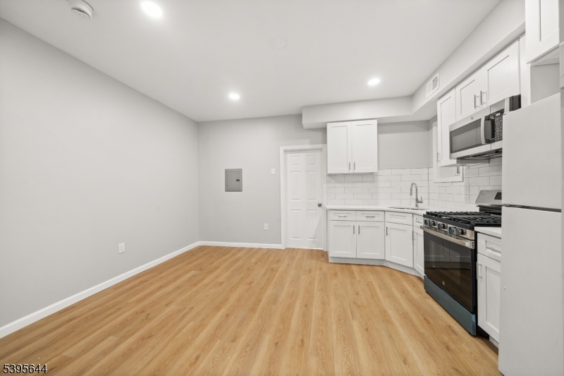 57 Henry Street, Unit A1 Passaic, NJ 07055 - Photo 3 of 14 a kitchen with granite countertop white cabinets stainless steel appliances and wooden floor