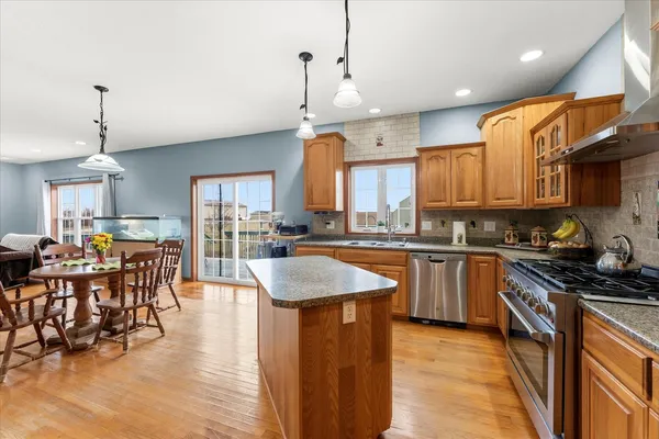 a kitchen with stainless steel appliances granite countertop a stove top oven a sink a dining table and chairs with wooden floor